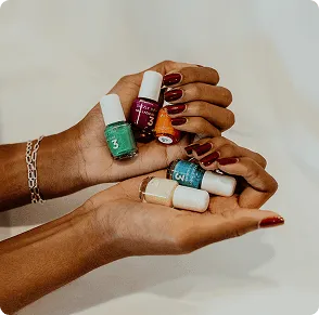 Two cupped hands holding several small colorful nail polish bottles, with a deep-red manicure visible