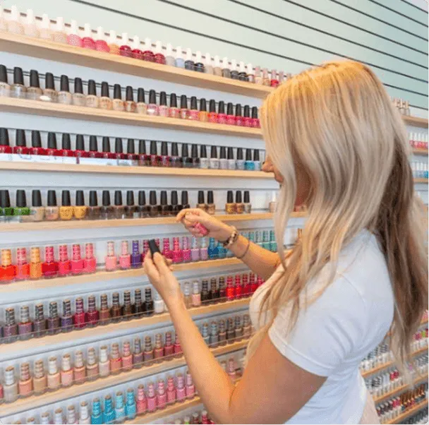 A woman browsing a floor-to-ceiling wall of colorful nail polish bottles